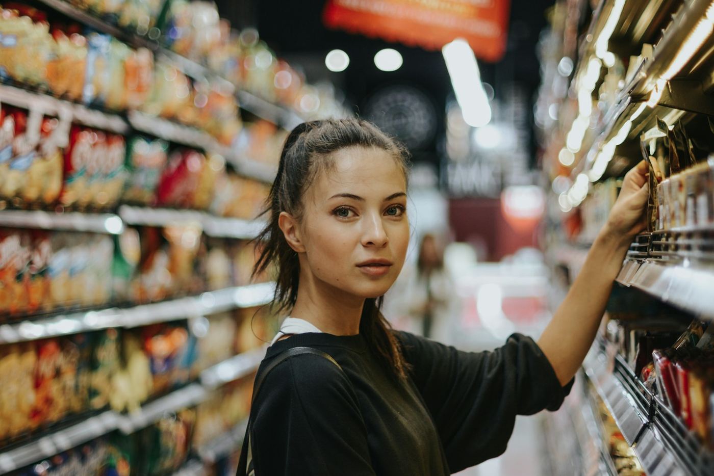 Kundin greift im Supermarktgang ins Regal